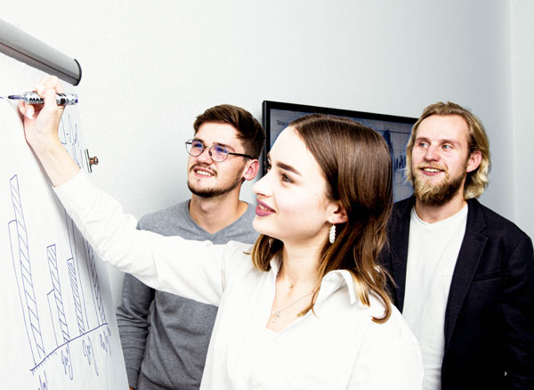 Drei junge Menschen in einem professionellen Umfeld vor einem Bildschirm mit Finanzdiagramm – Symbolbild für Nachwuchsförderung und Berufsorientierung in der Steuerberatung.